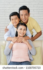 Loving Asian family of three gathered together at cozy living room and posing for photography with wide smiles, group portrait shot