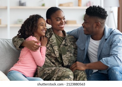 Loving attractive black woman in camouflage uniform mother having conversation with her family happy teen daughter and cheerful husband, sitting on couch all together and talking, home interior