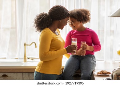 Loving Black Family Mother And Daughter Bonding While Having Snacks In Kitchen, Eating Homemade Cookies And Drinking Milk Together, Affectionate African Mom Touching Foreheads With Her Happy Kid