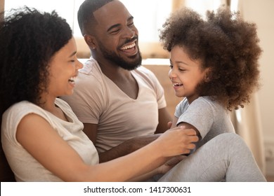 Loving Black Family Relaxing Bonding In Bedroom In The Morning, Happy African American Parents Laughing Cuddling Having Fun With Cute Little Kid Child Daughter Playing Enjoying Moments Together