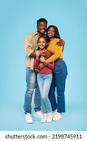 Loving black family of three embracing and smiling at camera, posing on blue background, studio shot, full length. Excited parents and their daughter hugging and expressing positive emotions - Shutterstock ID 2198745911