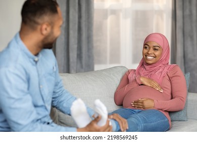 Loving black husband making foot massage for his pregnant muslim wife at home, helping her to relax, happy islamic spouses expecting baby resting on couch in living room together, free space - Powered by Shutterstock