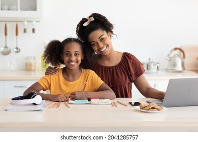 Loving Black Mother Helping Her Teen Daughter With Homework, Sitting Together At Kitchen Table In Front Of Laptop, Checking Notepad With School Notes, Having Online Lesson, Copy Space