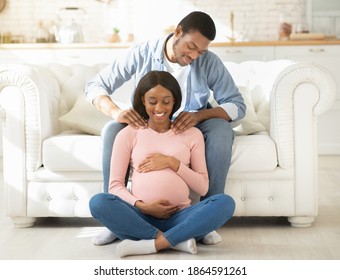 Loving boyfriend massaging his expectant girlfriend's shoulders at home, full length portrait. Tender African American man giving massage to his lovely wife to relieve tension during pregnancy - Powered by Shutterstock