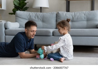 Loving Caring Millennial Dad And Cute Preschool Daughter Kid Playing On Heating Floor At Home, Making Tea Party With Toy Plastic Cups And Teapot, Talking, Interacting, Enjoying Game Activities