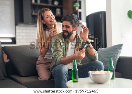 Loving caucasian couple playing. Man is holding joystick and trying to play video game while his girlfriend sits behind him and teases him