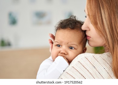 Loving caucasian young mother hugging soothing cute african american infant baby girl teething biting hand getting first tooth. Diverse mum and little child daughter bonding. Pediatric dental care.