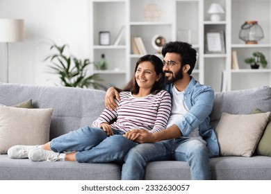 Loving cheerful eastern millennial man and woman in comfy casual outfit cuddling at home, happy sweet couple sitting on couch in living-room, embracing and looking at copy space. Domestic lifestyle - Powered by Shutterstock