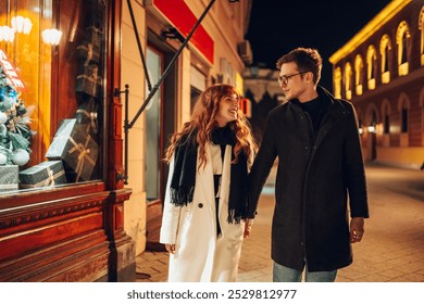 A loving christmas couple is holding hands and walking on city street downtown near store with christmas presents at new year's eve. An affectionate festive couple walking on street on christmas eve. - Powered by Shutterstock