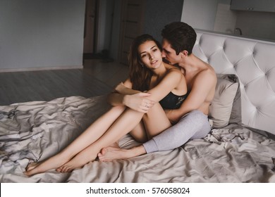 Loving couple in bed, woman sitting between the legs of men. Chemise made of black lace with a young woman. A man kisses her neck