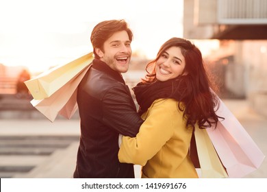 Loving couple carrying shopping bags and walking at sunset in city center