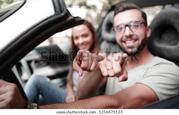 loving couple\
in a convertible car pointing at\
you