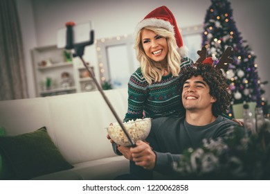 Loving couple in cozy warm sweaters on a Christmas - New Year eve, smiling and having fun taking selfie and eating popcorn.   - Powered by Shutterstock