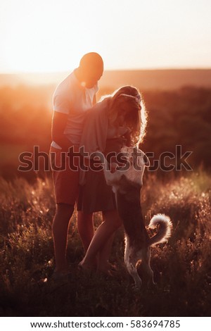 loving couple with a dog on the background of beautiful orange sunset