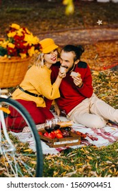 Loving Couple Eating Cheesy Snacks Sitting On A Mat In The Park. Autumn Picnic