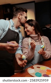 Loving couple embraces creativity while painting easter eggs at home. They share a tender moment, showcasing their artistic skills and enjoying quality time together in a cozy setting