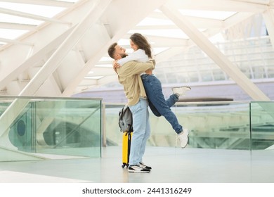 Loving couple embracing joyfully in the airport terminal, romantic man lifting woman off the ground, joyful spouses reunited after long time apart, happy to see each other, copy space - Powered by Shutterstock