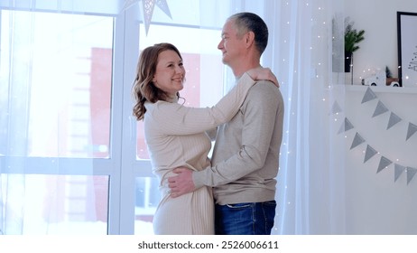 Loving couple is embracing next to their window on a cold winter day, enjoying the holiday season in their decorated home. A day with family before Christmas. New Year's Eve with family - Powered by Shutterstock