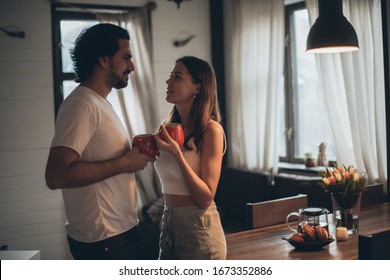 Loving couple in the evening in the living room at home. A young family is drinking tea, a girl is sitting on a table. Romantic family evening at home, dim light. - Powered by Shutterstock