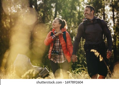 Loving couple going for a camping trip. Man and woman backpackers walking through forest holding hands and looking away.