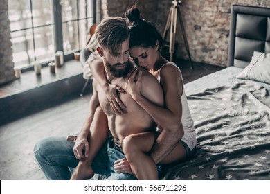 Loving couple. Handsome young hipster with beard and attractive woman resting at home while sitting on bed at home