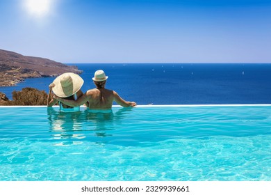 A loving couple with hats hugging at the edge of an infinity pool and enjoying the view to the blue, mediterranean sea during summer vacation time - Shutterstock ID 2329939661