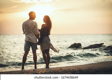 A loving couple is having fun and hugging on the empty sandy sea beach at sunset.They are looking each other and happily smiling. - Shutterstock ID 1674438649