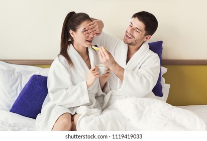 Loving couple having a lazy morning breakfast in comfortable bed. Husband feeding wife