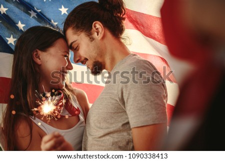 Loving couple holding sparklers wrapped under American flag. American man and woman celebrating independence day.