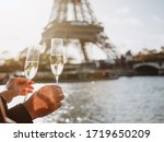 A loving couple holds in their hands glasses with expensive champagne against the background of the Eiffel Tower in Paris. The Eiffel Tower is reflected in champagne glasses. Romantic trip to Paris