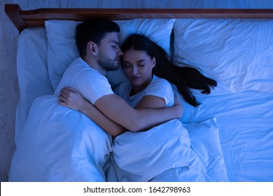 Loving Couple Hugging Sleeping Together Lying In Bed At Home At Night. Low Light, Above View