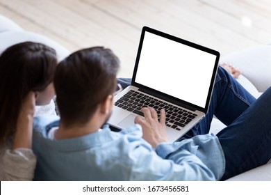 Loving couple looking at laptop screen blank white mockup close up, sitting on cozy sofa, young man and woman reading email, message, searching information in internet, shopping or chatting online
