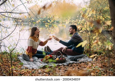 A loving couple on a date on a picnic on the lake. Young man and woman sit on a blanket with wine and fruits near the water in the park in autumn. A young family is celebrating an anniversary. - Powered by Shutterstock