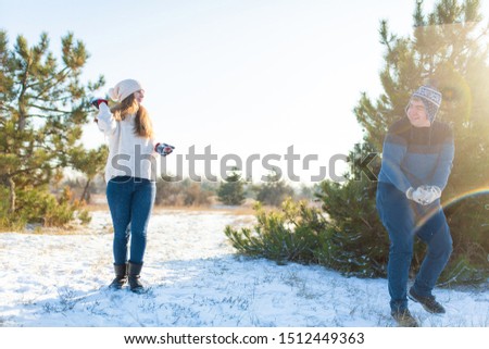 Loving couple play snowballs in winter in the forest. Throw each other snow. Laugh and have a good time.