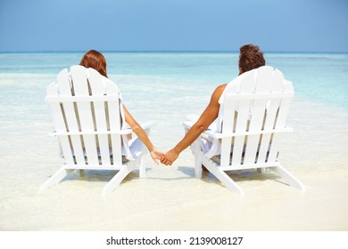 Loving couple relaxing on deck chairs. Rear view of loving couple holding hands while relaxing on deck chairs at seashore.