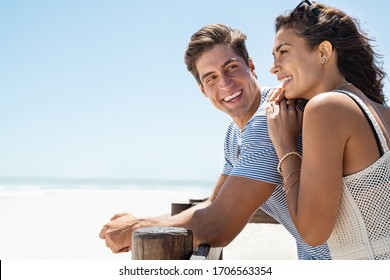 Loving couple standing at beach shore while looking away with copy space. Young man looking at beautiful woman on beach while she is contemplating the future. Boyfriend and girlfriend enjoying summer.