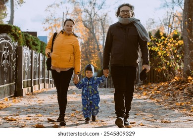 A loving couple strolls through a sunlit park with their young son, surrounded by the vibrant colors of autumn, enjoying a joyful and peaceful family moment together. - Powered by Shutterstock