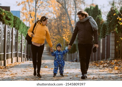 A loving couple strolls through a sunlit park with their young son, surrounded by the vibrant colors of autumn, enjoying a joyful and peaceful family moment together. - Powered by Shutterstock