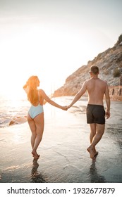 A loving couple walks along the beach by the sea. Young family at sunset by the Mediterranean Sea. Vacation concept. A woman in a swimsuit and a man in shorts at sunset by the sea. Selective focus.