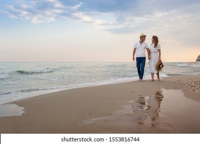 Loving couple walks along the sandy seashore at sunset