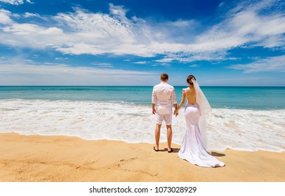 Loving Couple In Wedding Clothes Stand  On The Tropical Beach, To Hold Hands