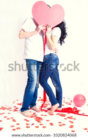 loving couple in white tank tops and blue jeans tied with red satin ribbon hugging in red rose petals     