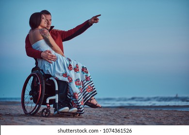 Loving couple, a woman sits on her husband's lap, resting on a beach against a background of a bright dawn. - Powered by Shutterstock