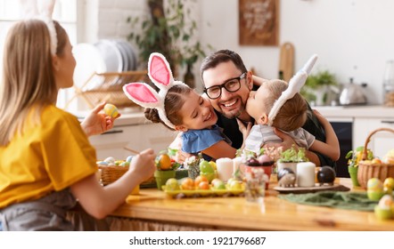 Loving cute children wearing funny bunny ears headbands embracing and kissing cheerful young father while gathering with family at table in kitchen for Easter eggs painting - Powered by Shutterstock