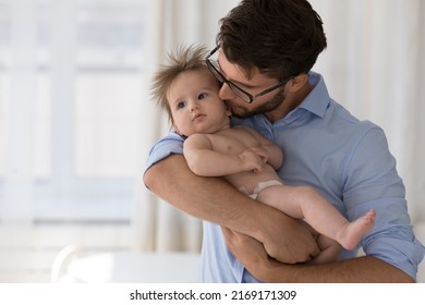 Loving Dad Kisses On Cheek His Adorable Baby, Standing At Home Holding On Arms Infant In Diaper Spend Time Together, Feeling Love, Express Caress And Care. Happy Fatherhood, Babyhood, Cherish Concept
