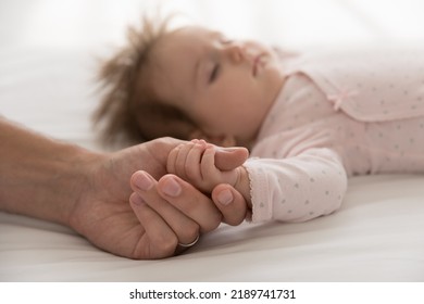 Loving Daddy Holds Tiny Arm Cute Sleeping Newborn Daughter, Baby Lying On Bed Touch Fathers Finger, Looks Calm, Fall Asleep At Home, Close Up. Family Ties, Paternal Love, Childcare, Adoption Concept