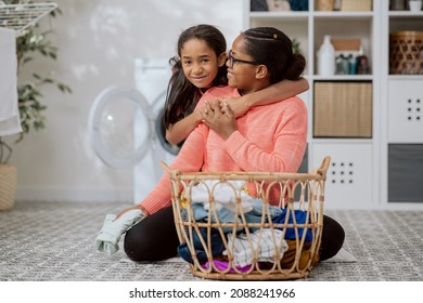 Loving Daughter Hugs Mom Who Sits On Laundry Room Floor, Bathroom Doing Household Chores, Sorting Laundry Into Washing Machine, Girl Thanks Woman