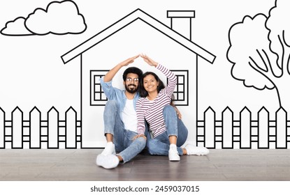 Loving eastern family husband and wife sitting over drawn on white wall house, make a roof with hands and smiling. Real estate, mortgage concept - Powered by Shutterstock