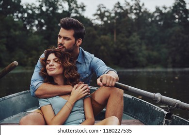 Loving everything about her. Beautiful young couple embracing and looking away while enjoying romantic date on the lake