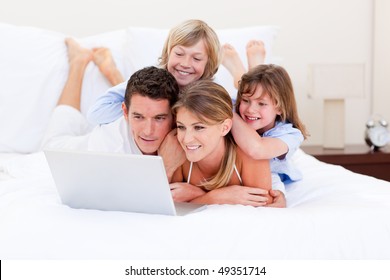 Loving family looking at a laptop lying down on bed at home - Powered by Shutterstock